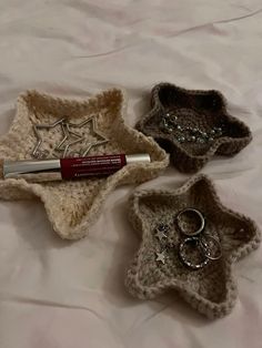 three small crocheted baskets with rings and lipstick in them sitting on a bed