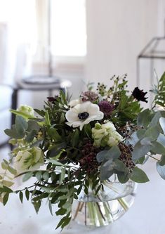 a vase filled with flowers and greenery on top of a table