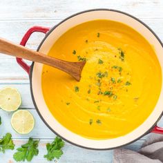 a red pot filled with yellow soup and garnished with parsley