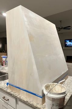 a large white object sitting on top of a kitchen counter next to a bucket of paint