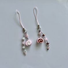 two pink and white beaded earrings with charms on the end are hanging from silver earwires