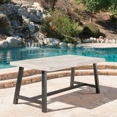 a table sitting on top of a stone patio next to a swimming pool with rocks