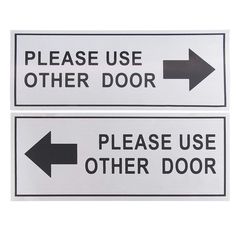 two black and white signs with arrows pointing in opposite directions, one says please use other door