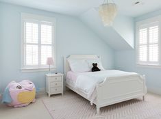 a white bed sitting under two windows in a bedroom next to a dresser and lamp