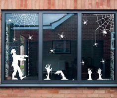 the window is decorated with white spider webs and silhouettes of people, bats, and zombies