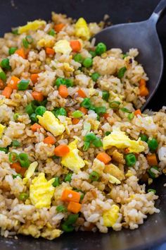 rice and vegetables are mixed in a skillet with a serving spoon on the side