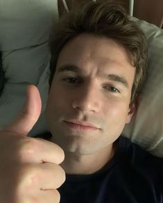 a man laying in bed giving the thumbs up sign with his hand and another person behind him