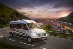 a white van driving down a road next to a lush green hillside