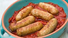 several sausages are in a blue bowl with tomato sauce on the side and one is cooked