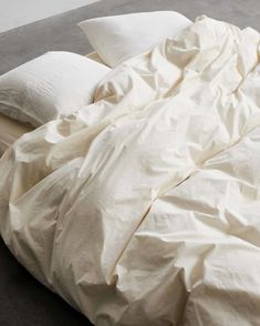 an unmade bed with white sheets and pillows on top of it, next to a wall