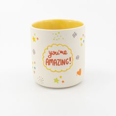 a yellow and white cup with the words you're amazing on it