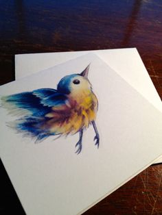 two cards with watercolor drawings of a bird on them sitting on a wooden table