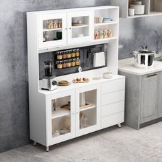 a kitchen with white cupboards and appliances on the counter top, next to a gray wall