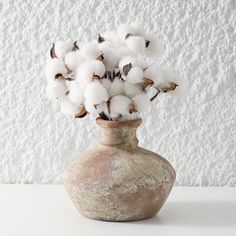 a vase filled with cotton sitting on top of a white table next to a wall