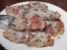 two pieces of meat covered in gravy on a white plate with a fork