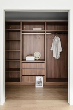 an open closet with wooden shelves and clothes hanging on the wall, next to a white basket