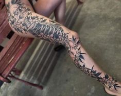 a woman's leg with tattoos on it and flowers in the middle, sitting on a bench