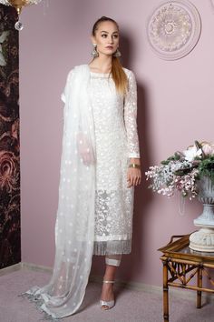 A delectable design that is delicately detailed with floral embroideries in shades of ebony and cream. Made with fully floral embroidered shirt front and sleeves high quality net fabric, embellished with unique tassel lace edging. Beautiful silk pants matched with organza patches. Paired with our luxurious white pure chiffon fabric that is layered with ornate embroidery all over the duppata and tassels on the pallus, this look creates an incandescent composition that will set your surroundings ablaze.  Top: Color: White      Fabric: Pure chiffon   Long shirt with floral embroidery all over    Sleeveless short undershirt    Full fitted sheer sleeves  Tassles dangling on border  Bottom: Color: White  Fabric: Silk   Slim pants with organza patch  Half elasticated waist  Dupatta:  Color: White Net Dresses Pakistani, Gharara Saree, Net Dress Design, Dresses Kurti, Indian Lengha, Dresses Pakistani, Wedding Pakistani, Luxury Pret, Pakistani Clothes