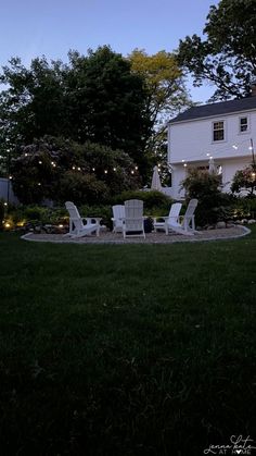 a backyard with lawn chairs and string lights on the side of the house at night