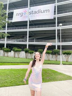 a woman is standing in front of a stadium holding her arm up to the sky