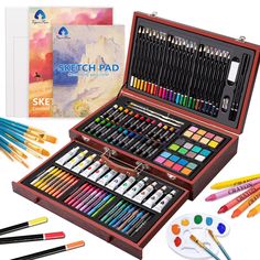 a wooden box filled with lots of different colored paints and pencils next to an art book