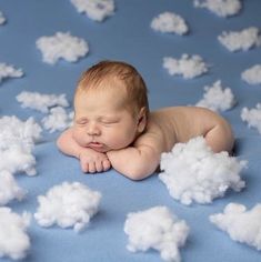 a baby is laying in the clouds with his head resting on his hands and eyes closed