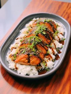 salmon and rice on a plate with sauce drizzled over the top, sitting on a wooden table