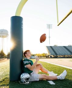 a man sitting on the ground with a football in his hand and another ball flying above him