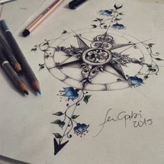 a compass tattoo design with blue flowers and leaves on paper next to some markers, pens and pencils