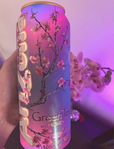 a person holding up a can of green tea with cherry blossoms on it in front of a purple background