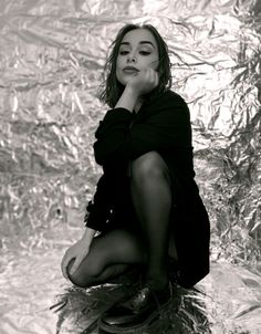 a woman sitting on top of a pile of tinfoil next to a wall with her hand under her chin