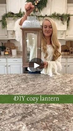 a woman standing in front of a kitchen counter holding an old fashioned lantern with the words diy cozy lantern on it