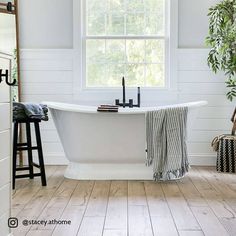 a white bath tub sitting under a window next to a wooden table and stools