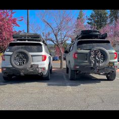 two vehicles parked next to each other in a parking lot with trees and flowers behind them