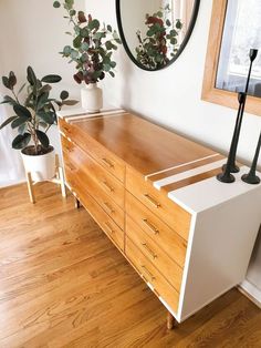 a wooden dresser sitting on top of a hard wood floor next to a mirror and potted plant