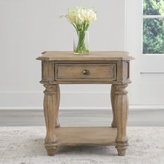 a small wooden table with flowers in a vase on the top and an area rug underneath it