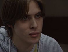 the young man is wearing a gray hoodie and looking to his left with an intense look on his face