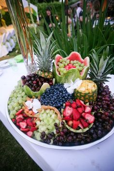 a large bowl filled with lots of different types of fruits and veggies on top of a white table