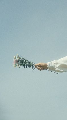 a man in white shirt holding flowers up to the sky with no clouds behind him