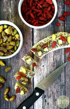 a knife and some food on a wooden table with bowls of nuts, raisins and pistachio