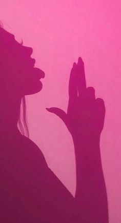 the silhouette of a woman holding her hand up in front of a pink sky background