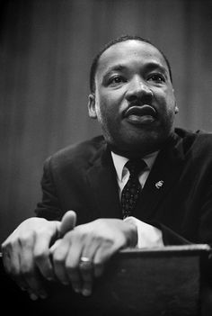 a black and white photo of a man in a suit with his hand on the desk