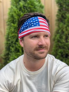 a man wearing an american flag headband in front of a wooden fence and bushes