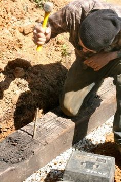 a man holding a hammer while working on a piece of wood in the dirt and gravel