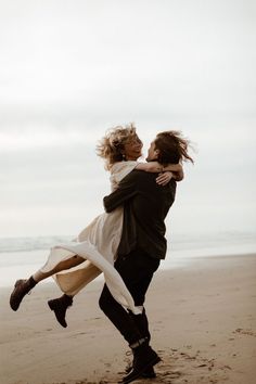 two people are hugging on the beach while one person holds his leg in the air