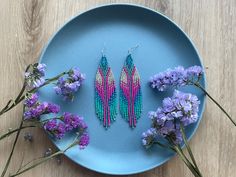 two pairs of beaded earrings sitting on a blue plate next to purple flower stems