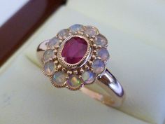 This gorgeous Ruby & Opal Vintage Inspired Flower Ring has been crafted from 9ct Solid Rose Gold. A bezel set oval cut NATURAL Ruby with surrounding NATURAL Opals brings this ring to life. Notice the stamens that surround the petals of this beautiful ring. This is an elegant Victorian inspired ring which simply looks beautiful on a lady who enjoys wearing fine jewellery from a Vintage era. THIS VINTAGE INSPIRED RUBY & OPAL RING IS TRULY AN EXQUISITE FINE JEWELLERY PIECE WHICH IS TO BE TR Luxury Victorian Cabochon Ruby Ring, 14k Gold Cluster Ring With Bezel Setting, Oval Shape, 14k Gold Cabochon Ruby Ring For Wedding, Ruby Cabochon Ring For Wedding, Heirloom Opal Ring With Bezel Setting For Anniversary, Oval Ruby Ring In Rose Gold With Bezel Setting, Victorian 14k Gold Jewelry With Bezel Setting, Opal Ring Vintage, Victorian Ring