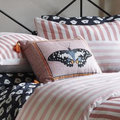 a bed with pink and white striped sheets, pillows and a butterfly pillow on it