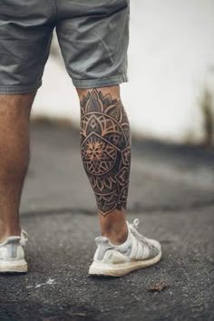 a man with a tattoo on his leg standing in the middle of an asphalt road