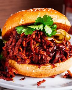 a pulled pork sandwich on a bun with pickles and cilantro garnishes